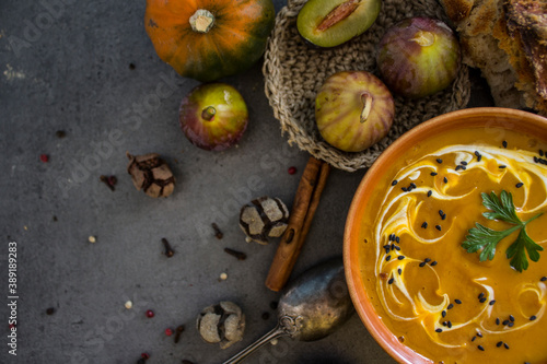 Autumn menu. Top view photo of bowl with pumpkin soup, gem squashes, rosemary, pepper, fresh baked bread and silver spoon. Dark grey textured background. Healthy eating concept. 