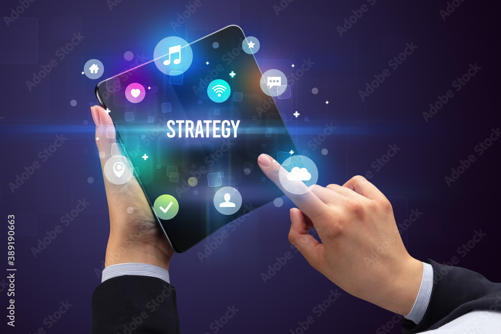 Obraz premium Businessman holding a foldable smartphone with STRATEGY inscription, social media concept