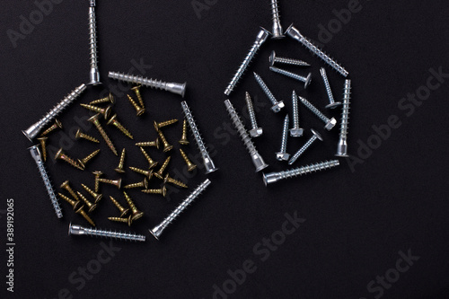Abstract shapes and background for text made of self-tapping screws and furniture screws on a black background (top view).