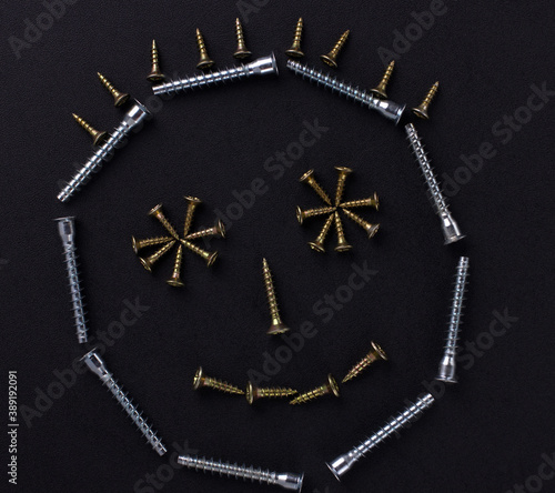 The outline of a smile is made of self-tapping screws on a black background (top view).