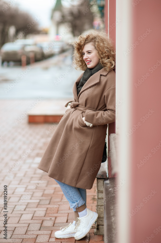 Portrait of a smiling young woman with curly hair. Outside. Girl standing leaning against the wall Portrait of a smiling young woman with curly hair. Outside. Girl standing leaning against the wall