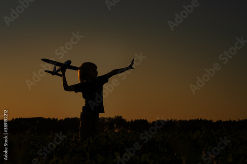 Silhouette of boy playing with airplane in the field