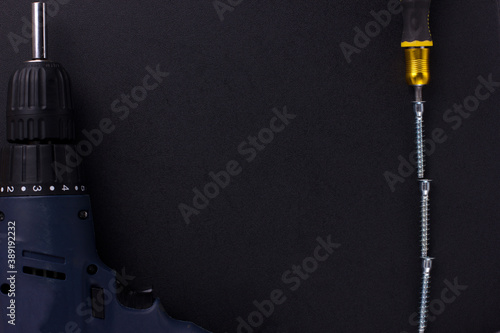 the background for the text is made of furniture screws, a screwdriver, a screwdriver on a black background (top view).