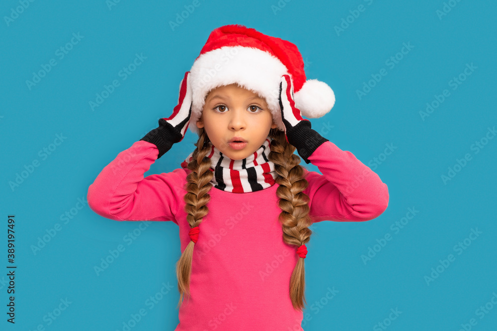 A little girl in a Christmas hat poses on a blue background for the new year. A little girl in a Christmas hat poses on a blue background for the new year.