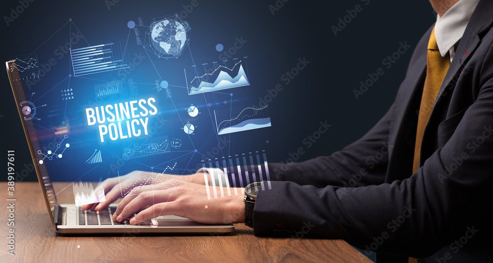 Businessman working on laptop with BUSINESS POLICY inscription, new business concept Businessman working on laptop with BUSINESS POLICY inscription, new business concept