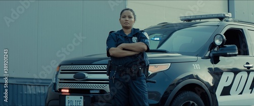 фотографія Mixed race female police officer posing against police car with flashing lights