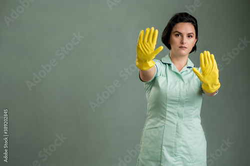 Young cleaning woman wearing a green shirt and yellow gloves showing stop sign © Cipri Suciu 