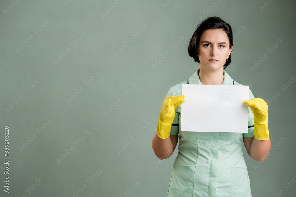 Young cleaning woman wearing a green shirt and yellow gloves holding a white paper Young cleaning woman wearing a green shirt and yellow gloves holding a white paper