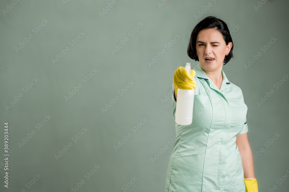 Young cleaning woman wearing a green shirt and yellow gloves holding window cleaning solution in hands Young cleaning woman wearing a green shirt and yellow gloves holding window cleaning solution in hands