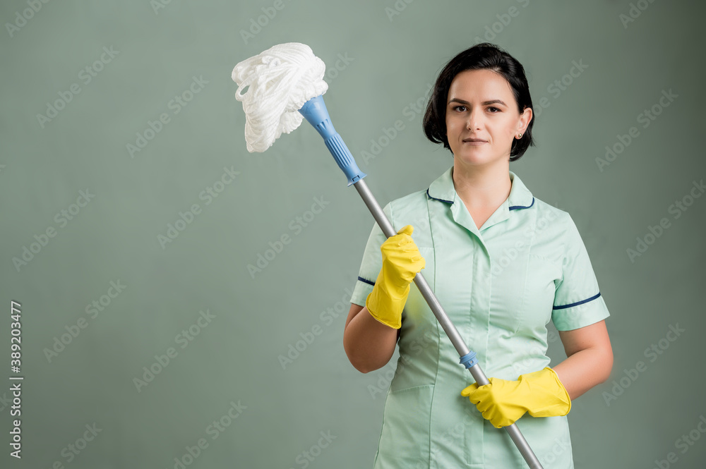 Young cleaning woman wearing a green shirt and yellow gloves holding mop