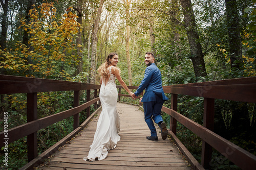 Foto Back view of a newly married couple running and looking back over a bridge in the woods