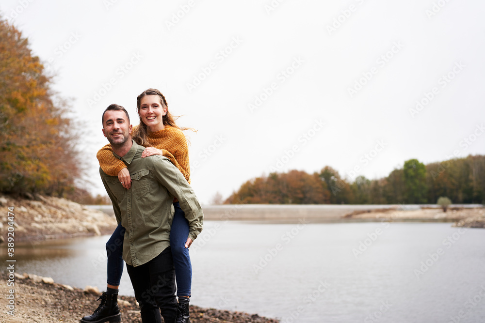 Young man piggibacking his girlfriend and laughing at the lake. Young man piggibacking his girlfriend and laughing at the lake.