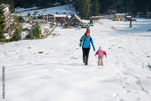 Mother and daughter walking up a ski slope.