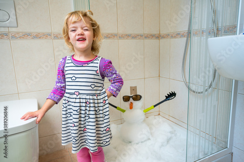 Happy girl building a snowman inside a shower. photo