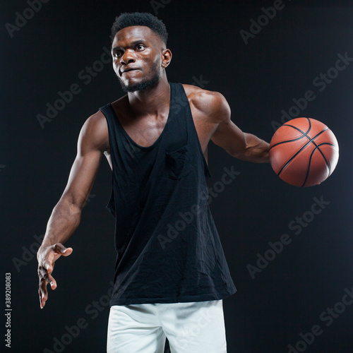Portrait of afro american male basketball player playing with a ball over black background. Fit young man in sportswear holding basketball © satyrenko