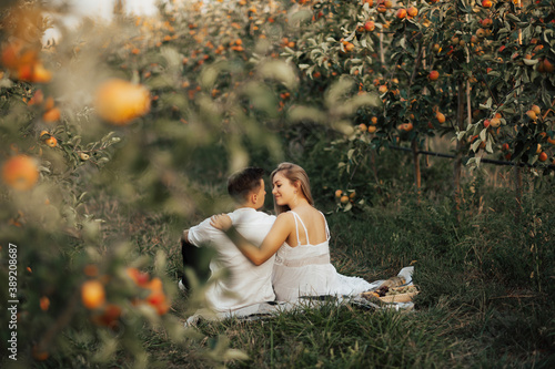 Obraz na płótnie Back view of happy couple is having a picnic in the apples garden. Cute young couple on picnic during romantic date outdoors. w salonie