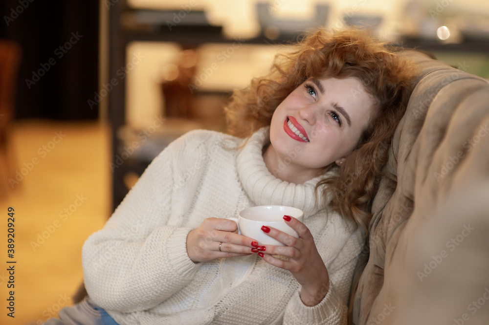 A beautiful girl sits in a cafe with a white cup in her hands and dreams. Inside A beautiful girl sits in a cafe with a white cup in her hands and dreams. Inside
