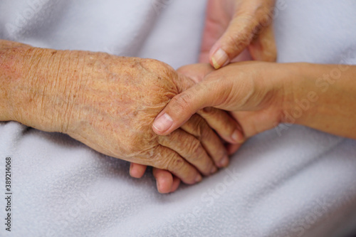 Touching or holding hands asian senior or elderly old woman on a blue cloth with love, care, encourage and empathy.