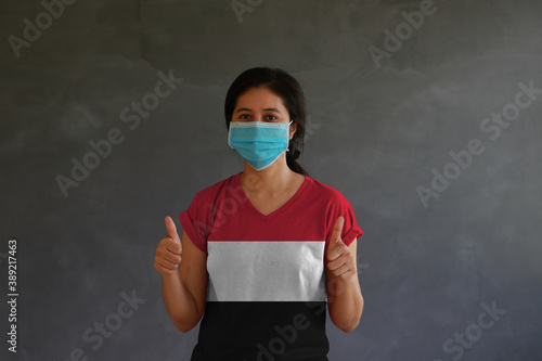 Woman wearing hygienic mask and wearing Yemen flag colored shirt with thumbs up with both hands photo