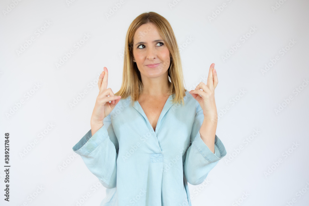 Portrait of a smiling young woman standing over white background, holding fingers crossed for good luck Portrait of a smiling young woman standing over white background, holding fingers crossed for good luck