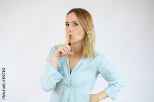 Young woman standing over isolated white background asking to be quiet with finger on lips. Silence and secret concept.