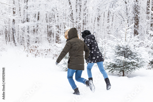 A young and beautiful couple is having fun in the snowy park, running and holding hands. Valentine's Day concept. Winter season.