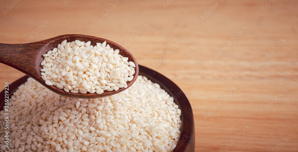 White sesame seeds in a wooden spoon and bowl focus on the spoon on the table,, organic food concept. White sesame seeds in a wooden spoon and bowl focus on the spoon on the table,, organic food concept.