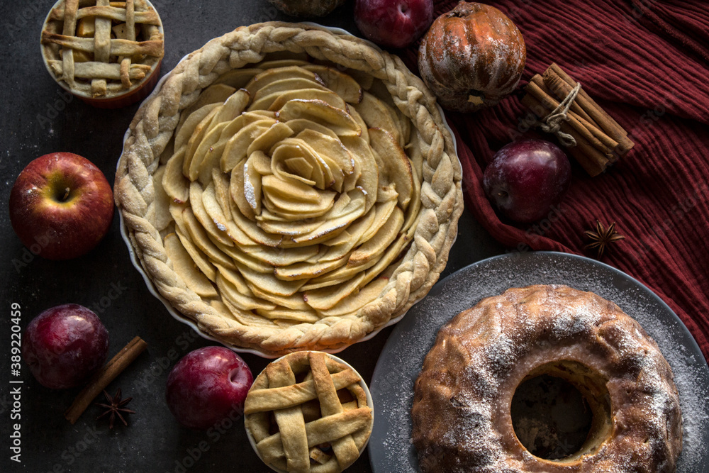 Lattice apple pie top view photo. Still life with different pastries. Apple cake, lattice apple pie. fresh plums and apples. pumpkins and cinnamon sticks on a table. Grey background with copy space. A