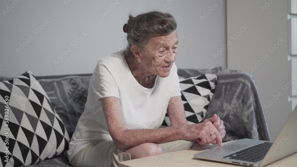Senior woman using laptop at home. Elderly people learning modern technology. Smiling senior woman waving with hand while having video call on laptop. Senior lifestyle. Mature woman using internet Senior woman using laptop at home. Elderly people learning modern technology. Smiling senior woman waving with hand while having video call on laptop. Senior lifestyle. Mature woman using internet