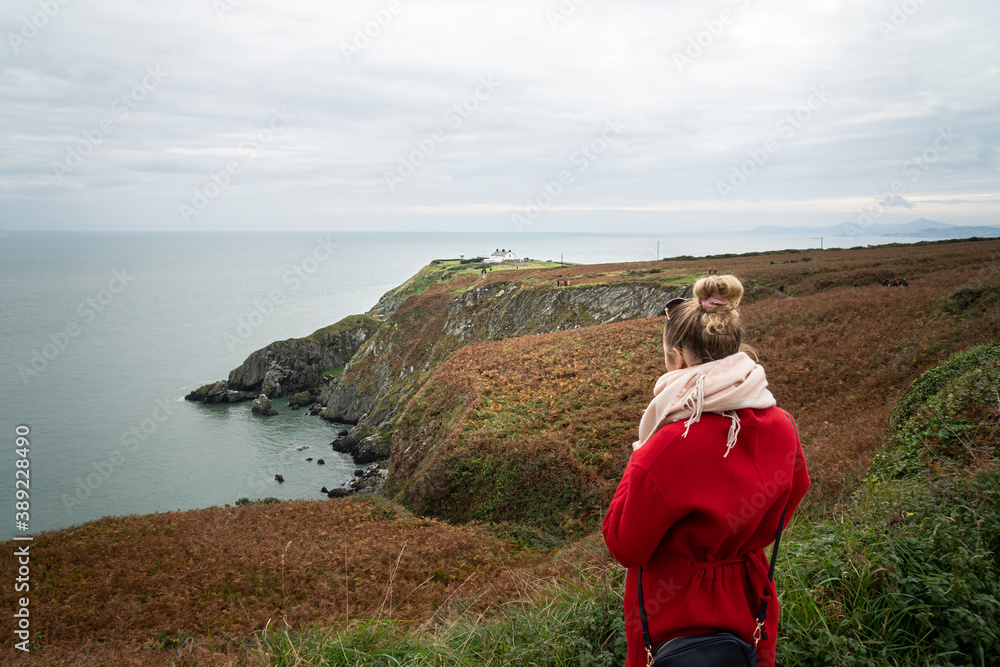 Fototapeta premium Beautiful scenery of Baily Lighthouse on Howth Head, county Dublin, Ireland. Girl in red coat in foreground