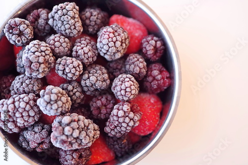 Frozen fruit berries in a pot on white background. Close-up with dark purple blackberries and red strawberries and raspberries. Ready to make homemade jam.