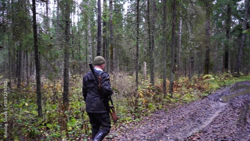 Hunter with a gun walks along a forest road Hunter with a gun walks along a forest road