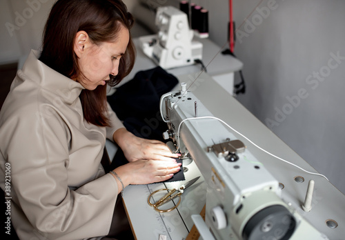 A woman sews a dark fabric on a sewing machine. Design studio, tailoring process concept.