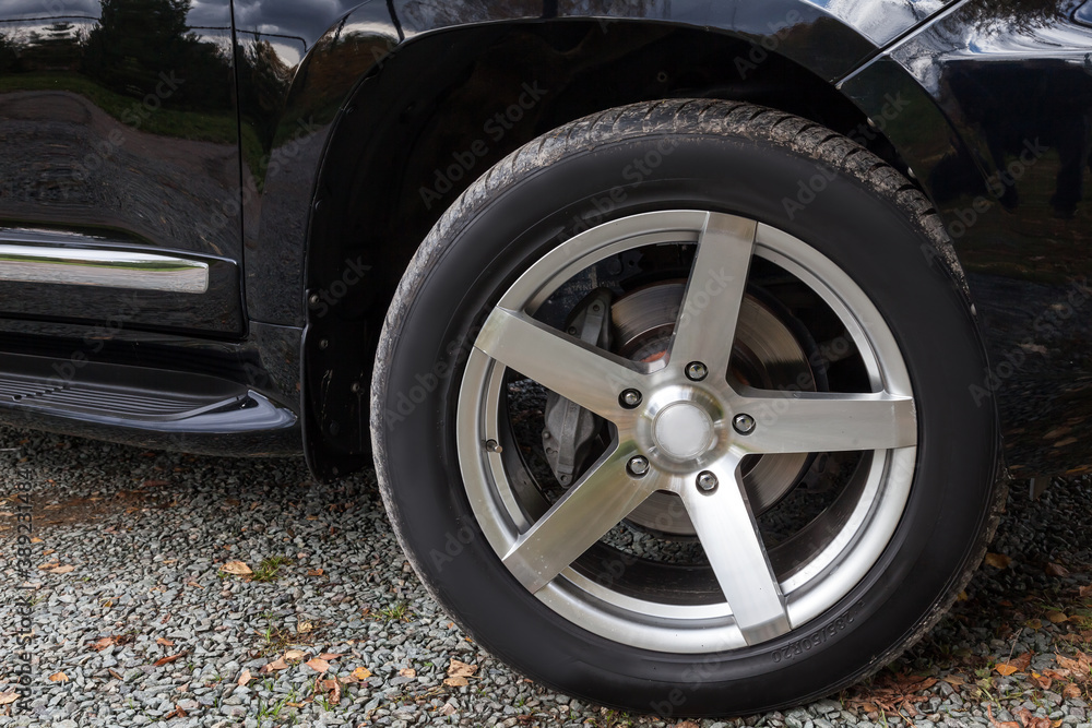 Close-up of a car wheel with black brake pads with a chrome rim and a black tire on a gravel road on an autumn day after replacing a summer chaff.