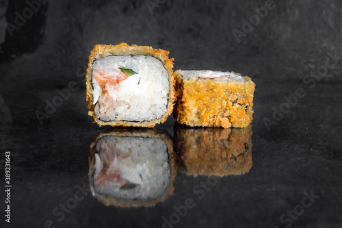 Tempura rolls with salmon, cucumber, eel and cream cheese on a dark background with reflection
