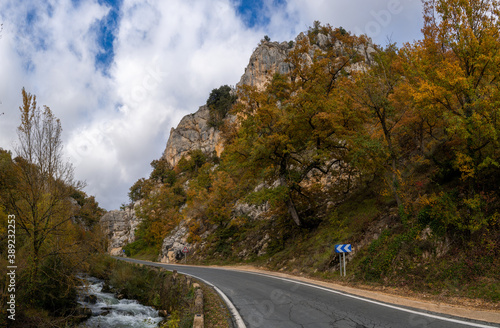 fall color forest and rocky cliffs with a winding mountain road next to a small river