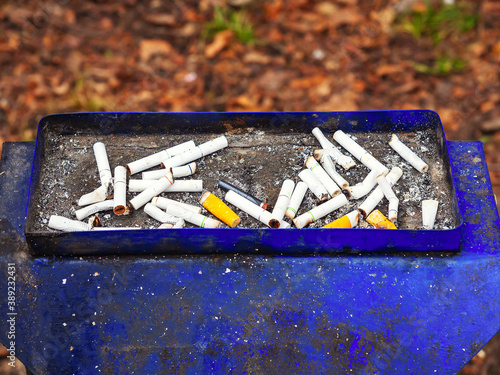 Blue shabby dirty street ashtray with many cigarette butts photo