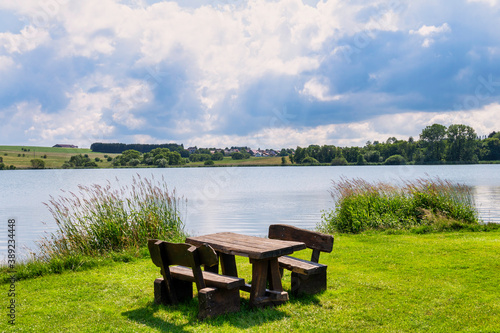 Picknickbank mit Tisch am See im Hintergrund Hügel und Bäume im Sommer 