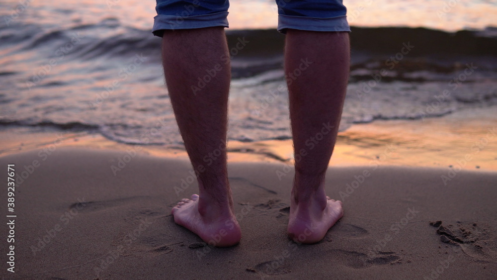 A man on a sandy shore slowly walks into the water A man on a sandy shore slowly walks into the water
