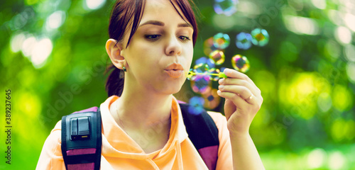 Young woman blowing bubbles on nature. Happy young brunette woman strolls in the Park and makes soap bubbles on a Sunny day