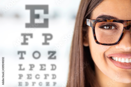 Close up of young woman wearing eyeglasses with eyechart in the background. Eyewear. Female children's doctor near eye chart in hospital. Young woman on eyesight test chart closeup