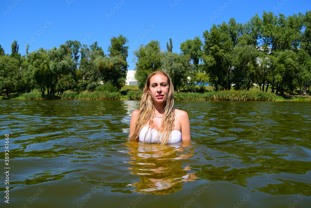 Fototapeta premium Young woman in the water on the lake near the forest