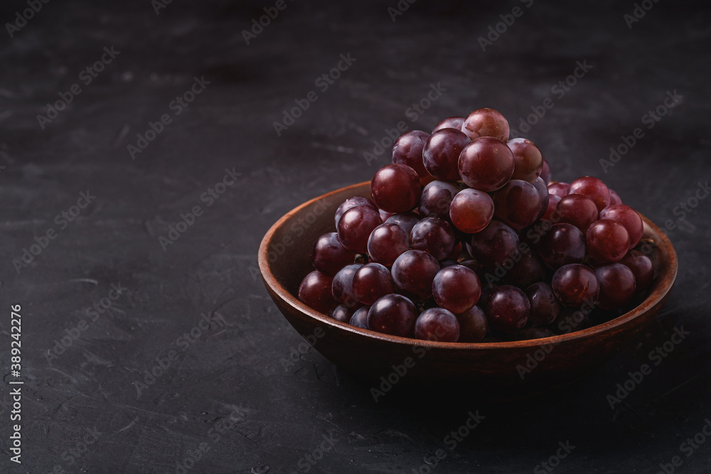Fresh ripe grape berries in brown wooden bowl on dark stone background, angle view Fresh ripe grape berries in brown wooden bowl on dark stone background, angle view