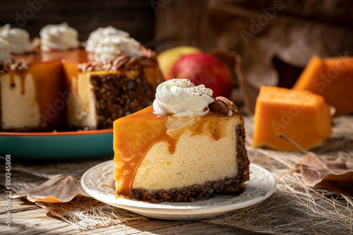 Pumpkin cheesecake. Curd cake with caramel, nuts, whipped cream, pumpkin, apples and autumn leaves on the background.