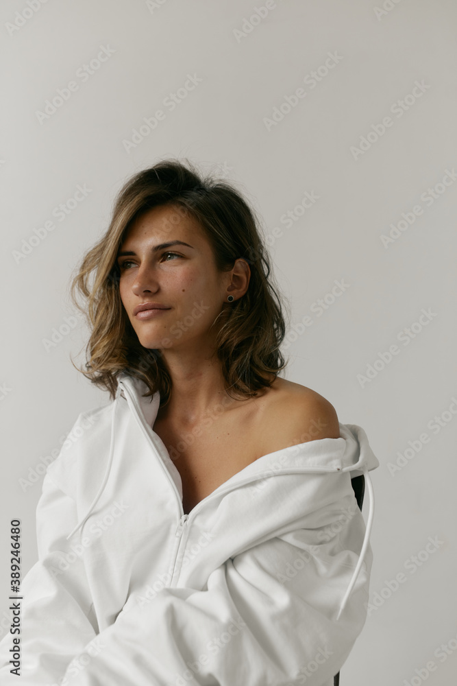Portrait of beautiful young woman with brown hair and clean bronze skin without makeup on white background. Natural and healthy look. Neutral interior. Soft light. Portrait of beautiful young woman with brown hair and clean bronze skin without makeup on white background. Natural and healthy look. Neutral interior. Soft light.