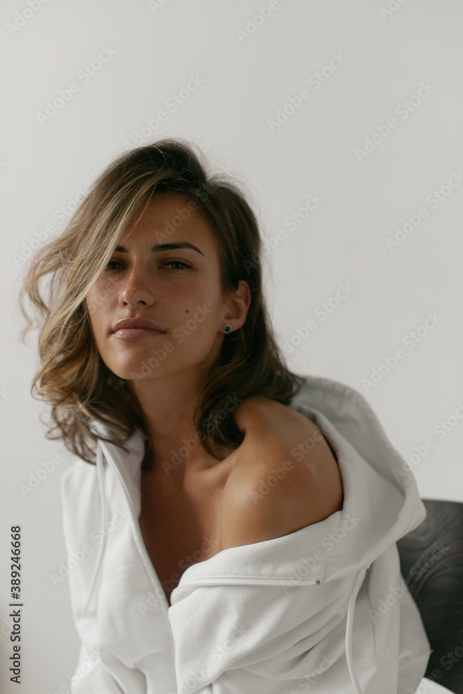Portrait of beautiful young woman with brown hair and clean bronze skin without makeup on white background. Natural and healthy look. Neutral interior. Soft light. Portrait of beautiful young woman with brown hair and clean bronze skin without makeup on white background. Natural and healthy look. Neutral interior. Soft light.