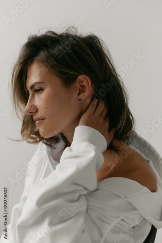 Portrait of beautiful young woman with brown hair and clean bronze skin without makeup on white background. Natural and healthy look. Neutral interior. Soft light. 