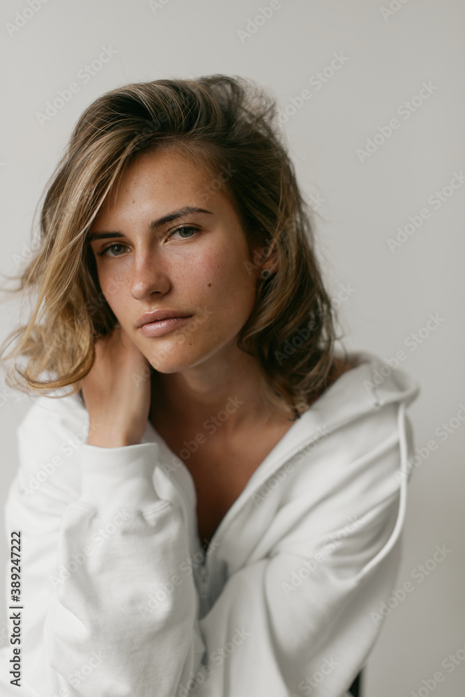 Portrait of beautiful young woman with brown hair and clean bronze skin without makeup on white background. Natural and healthy look. Neutral interior. Soft light. Portrait of beautiful young woman with brown hair and clean bronze skin without makeup on white background. Natural and healthy look. Neutral interior. Soft light.