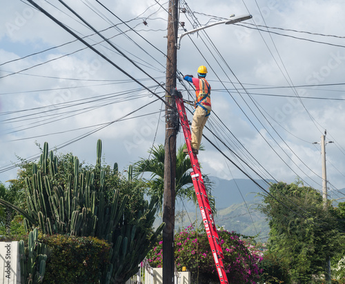 low angle shot of an electrician working from a ladder high up on a utility pole on a bright sunny day