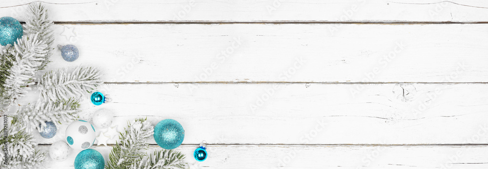 Fototapeta premium Christmas corner border of frosty branches with blue and white decorations. Overhead view on a white wood banner background with copy space.